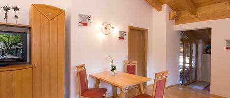 Un comedor con una mesa y sillas de madera, un televisor sobre un mueble, y una puerta que da a otra habitación.
