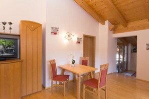 Uma sala de jantar com mesa e cadeiras de madeira, televisão em um móvel e porta que dá para outro cômodo.