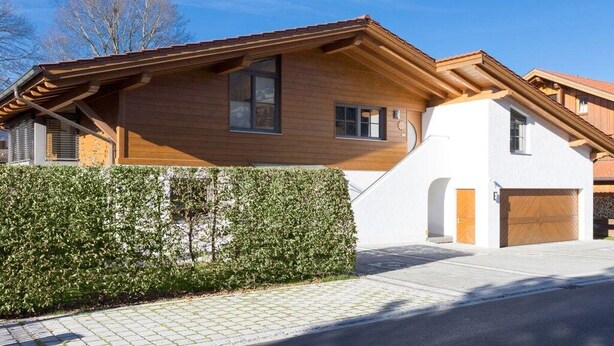 A modern two-story house with a wooden facade, a garage, and a well-maintained hedge. - Holiday apartment with 1 bedroom (Oberammergau)
