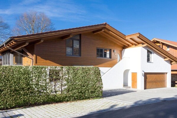 Uma casa moderna de dois andares com fachada de madeira, garagem e um hedge bem cuidado.