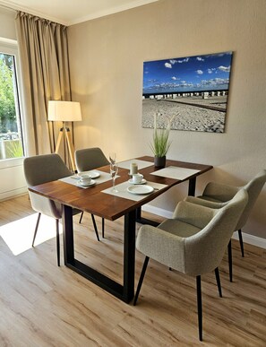 Ein Essbereich mit einem Holztisch, vier Stühlen, einer Topfpflanze und einem Strandbild an der Wand.