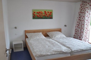 A bedroom with a wooden bed, a small bedside table, and a painting of red flowers on the wall. - Holiday apartment in Salem with swimming pool (Salem)