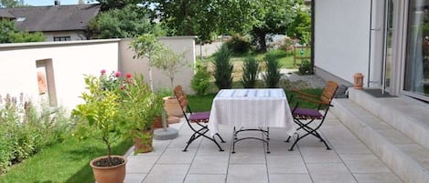 Um pátio com mesa e cadeiras, cercado por vasos de plantas e gramado.