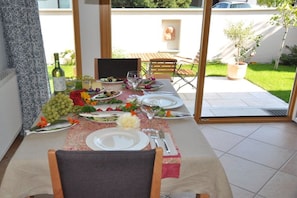 A dining table set for four with plates, cutlery, and a bottle of wine, overlooking a garden. - Holiday apartment in Salem with swimming pool (Salem)