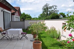 A patio with a table and chairs, a potted plant, and a small garden area with grass and shrubs. - Holiday apartment in Salem with swimming pool (Salem)