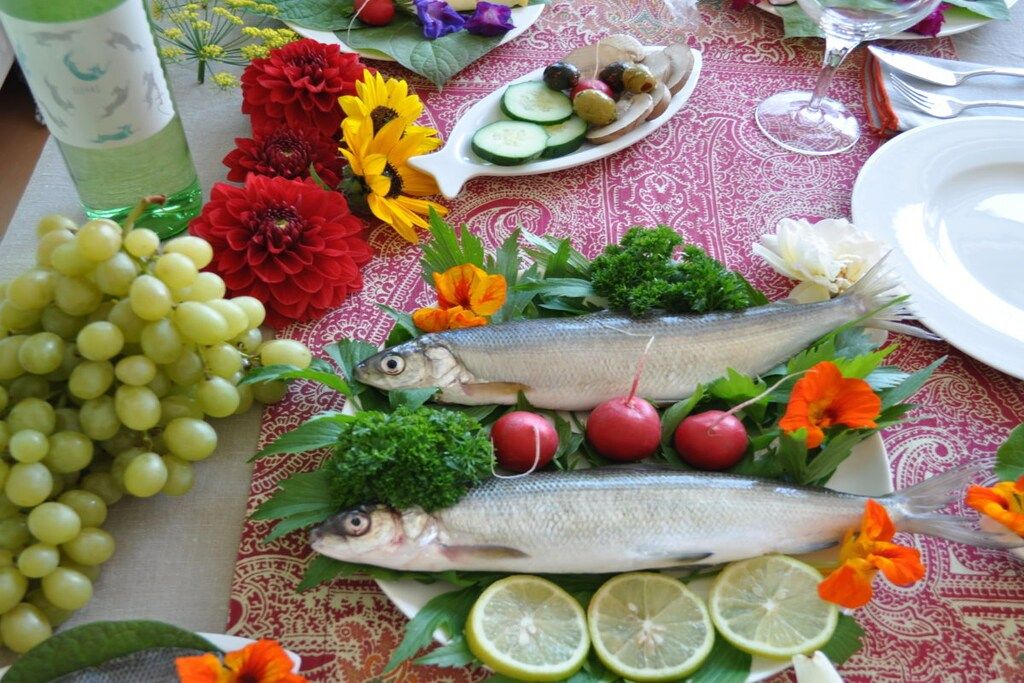 A table with fish, grapes, flowers, and a bottle.