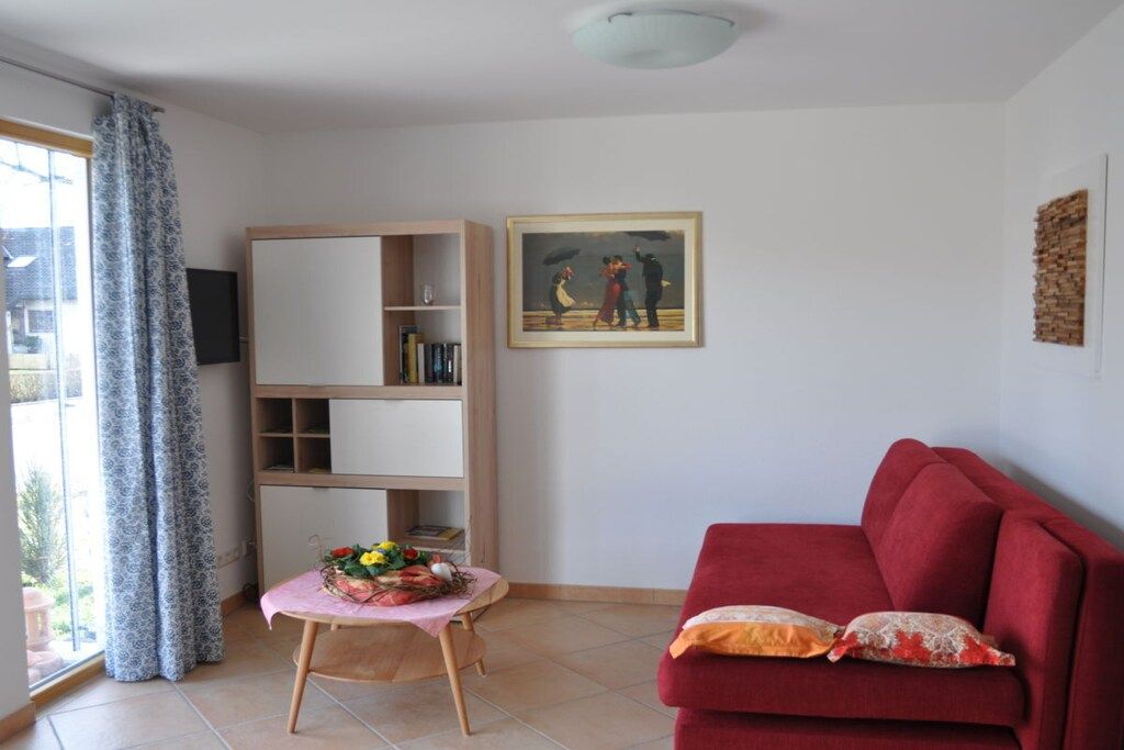 Ein Wohnzimmer mit einem roten Sofa, einem hölzernen Bücherregal, einem kleinen Tisch mit Blumen und einem Gemälde an der Wand.