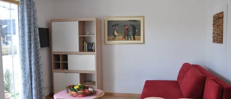 Ein Wohnzimmer mit einem roten Sofa, einem hölzernen Bücherregal, einem kleinen Tisch mit Blumen und einem Gemälde an der Wand.