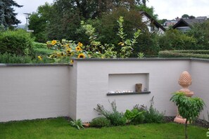 Ein Garten mit einer weißen Mauer, einem Regal mit Dekoration und einem Blumentopf.