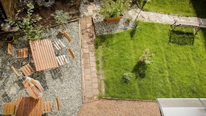 Un jardín en la azotea con terraza de madera, un pequeño césped y una banca.