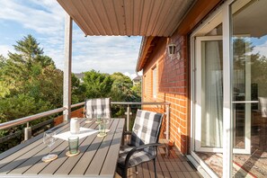 Eine Holzterrasse mit Tisch, Stühlen und einem Weinglas.
