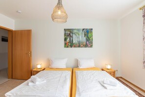 Ein Hotelzimmer mit zwei Betten, einem Waldgemälde und einer Pendelleuchte.