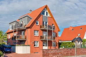 Ein mehrgeschossiges Wohngebäude mit roter Backsteinfassade, Balkonen und blauem Himmel.