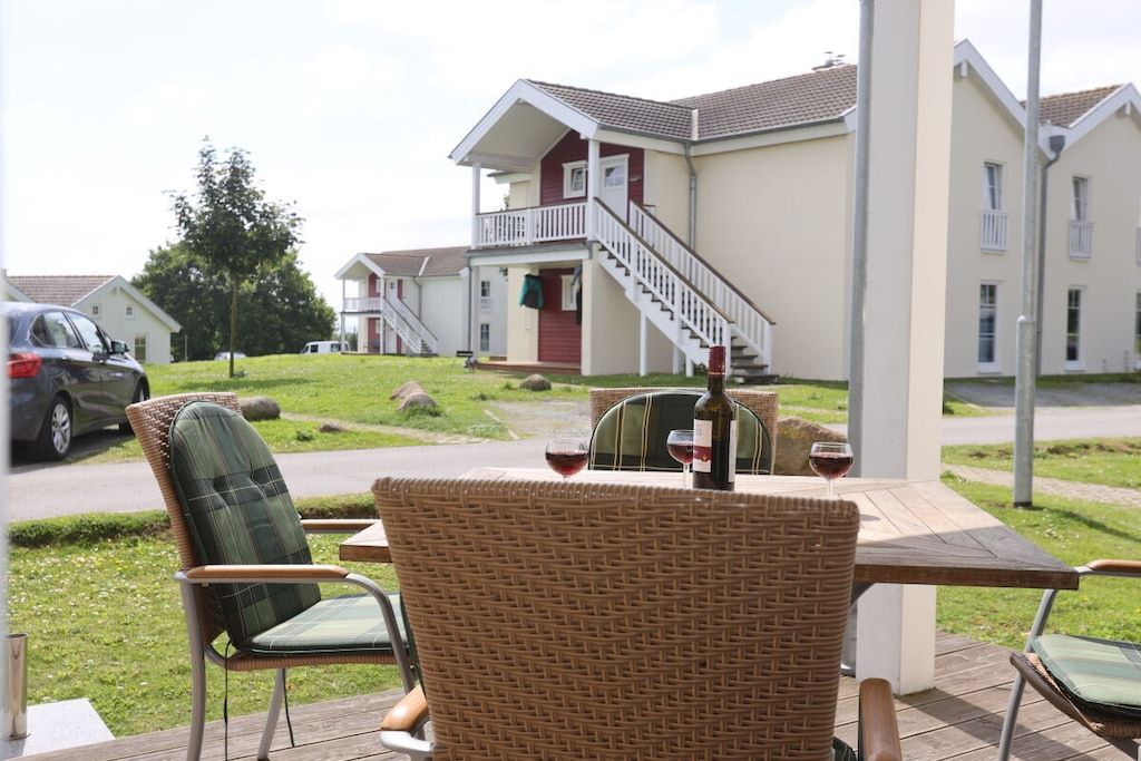 Een terras met rieten stoelen en een tafel, een trap naar een gebouw en een geparkeerde auto.