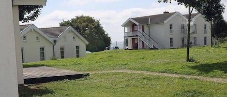 A row of white houses with a grassy yard and a wooden deck.