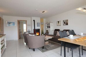 A modern living room with a fireplace, a dining area with a table and chairs, and a sofa. - Holiday apartment with 2 bedrooms (Sierksdorf)