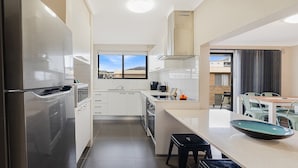 A modern kitchen with stainless steel appliances, a window with a view, and a dining area with a table and chairs. - Pacific Court 10 by HolidayCo. (THE ENTRANCE)