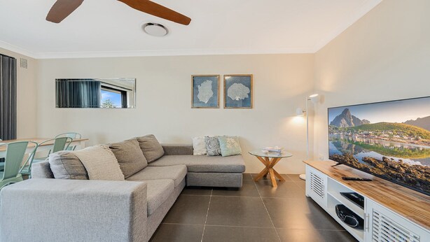 A modern living room with a sectional sofa, a glass coffee table, and a flat-screen TV on a wooden stand. - Pacific Court 10 by HolidayCo. (THE ENTRANCE)