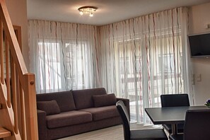 A living room with a sofa, a dining table, and a TV mounted on the wall. - Holiday apartment with 1 bedroom (Vogtsburg-Oberbergen)