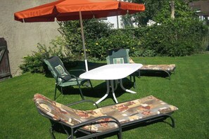An outdoor patio with a table and chairs, a large umbrella, and a lawn. - Holiday apartment with 1 bedroom (Vogtsburg-Oberbergen)