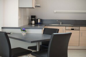 A modern kitchen with a dining area, featuring a table with chairs, a coffee machine, and a sink. - Holiday apartment with 1 bedroom (Vogtsburg-Oberbergen)