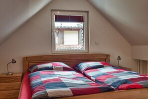 Un dormitorio con techo inclinado, una ventana con persianas, una cama de madera con colcha a rayas y lámparas de noche.