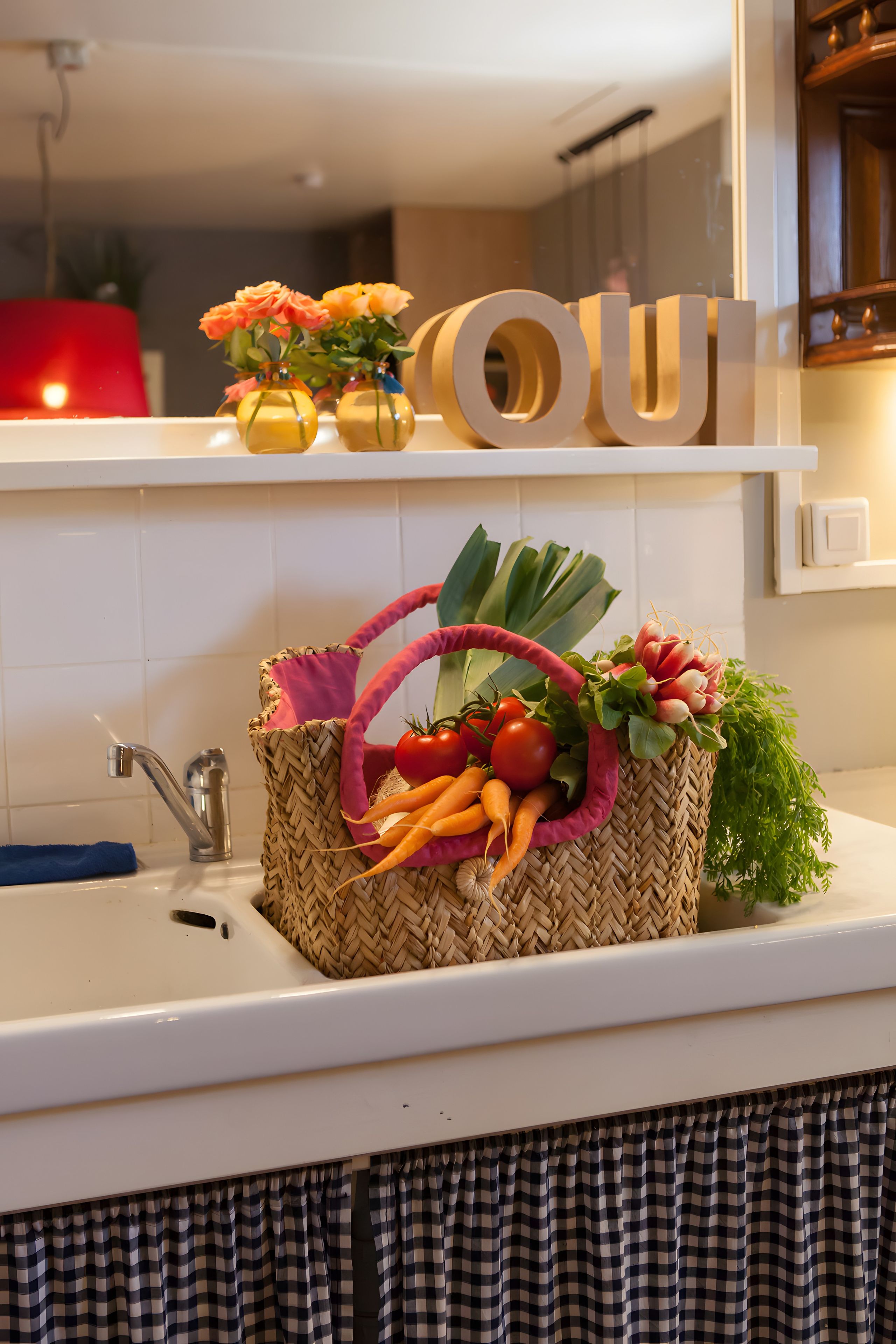A kitchen with a sink, a woven basket with vegetables, and a 'OU' sign on the wall.