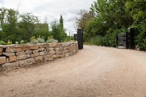 A gravel driveway leading to a stone wall with a gate. - Le Petit Chateau: house with private pool, Wi-Fi and air conditioning (Bétaille)