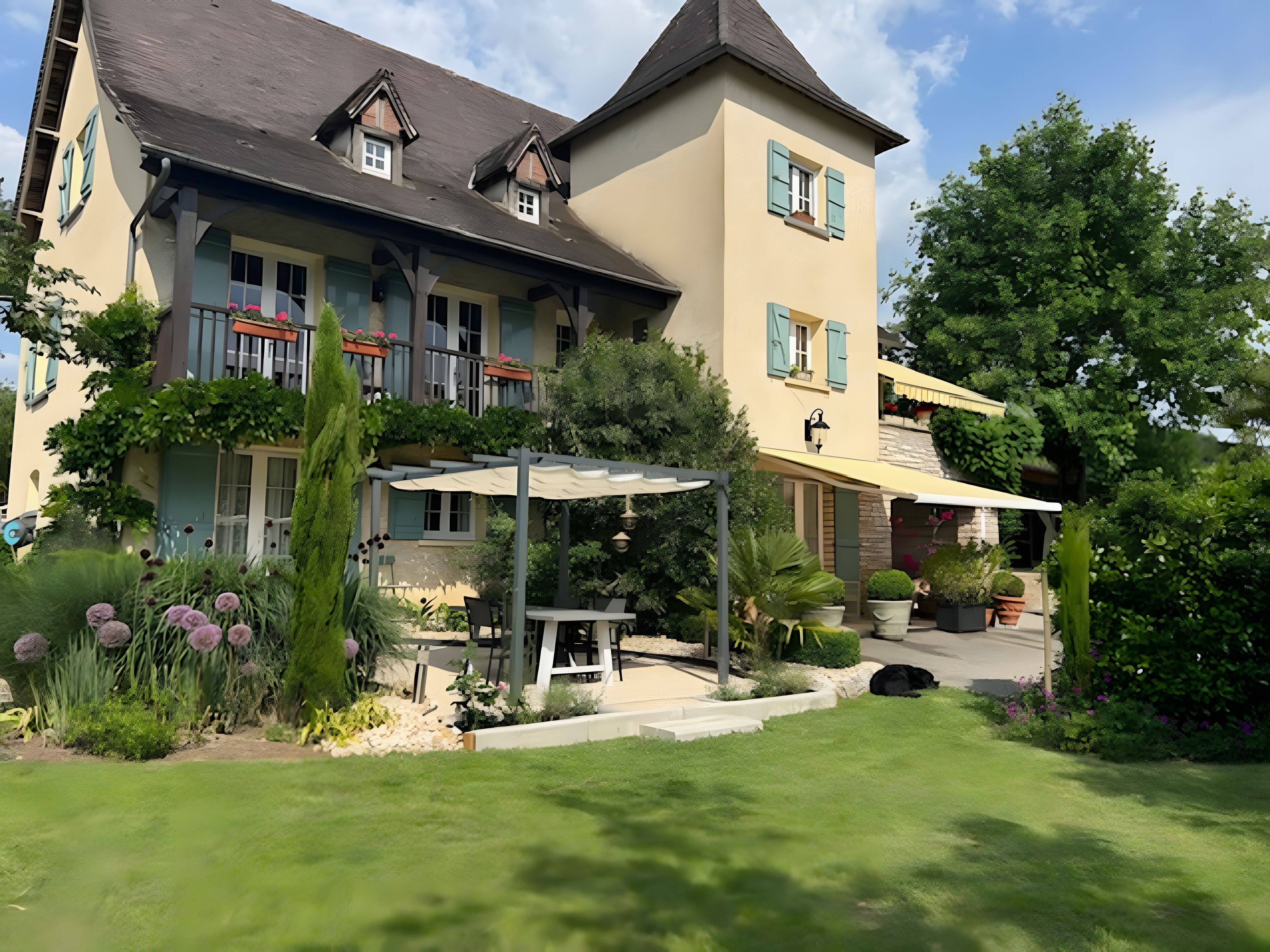 Ein zweistöckiges Gebäude mit überdachter Terrasse, einem kleinen Garten mit Kübelpflanzen und einer Sitzecke.