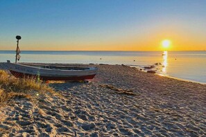 A boat on a sandy beach with calm water and a sunset in the background. - Holiday apartment with 1 bedroom (Sierksdorf)