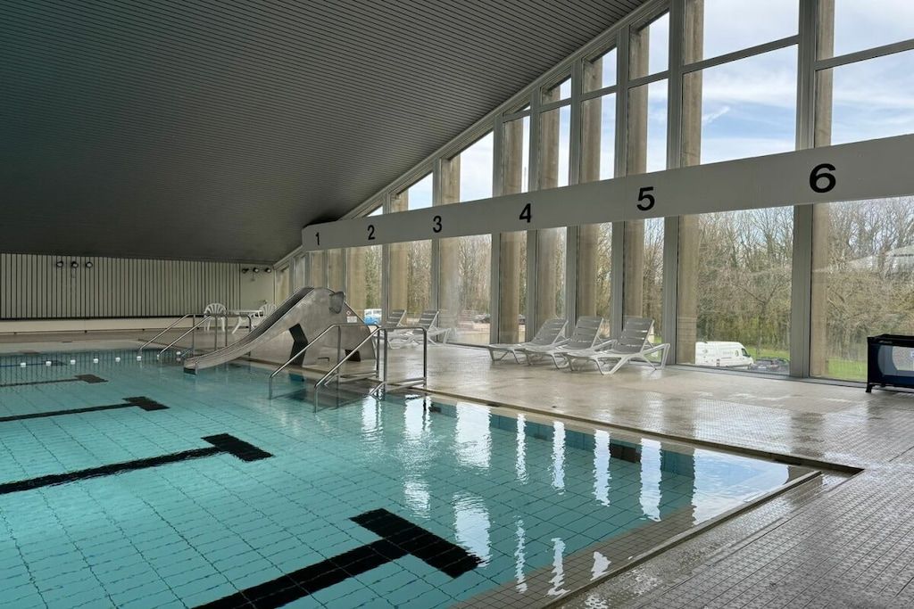 Une piscine intérieure avec des couloirs numérotés, un toboggan et des chaises longues.