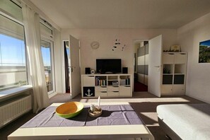 Een moderne woonkamer met een flatscreen televisie, een boekenkast en een eettafel met een schaal en kaars.