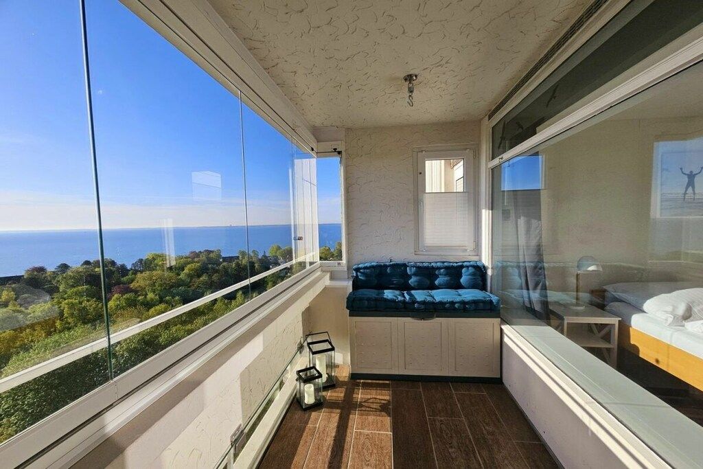 Un balcón con vista al mar, una zona de estar con cojines y una cama con cabecera.