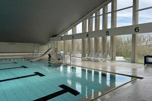 Ein Hallenbad mit Bahnen, einer Rutsche und Liegestühlen.