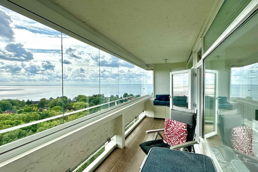 Un balcón con vista al mar y vegetación, una silla y una mesita.