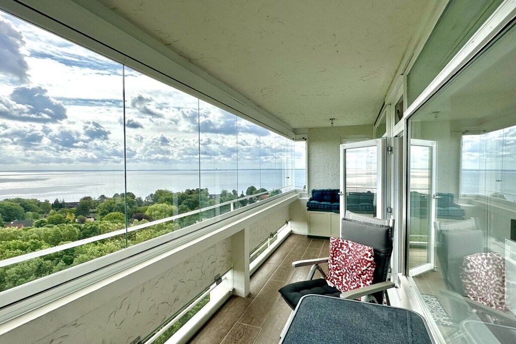 Un balcón con vistas al mar y vegetación, una silla y un sofá.