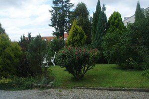 A garden with various trees and shrubs, a white chair, and a building in the background. - Villa Maja Lake Constance (Markdorf)