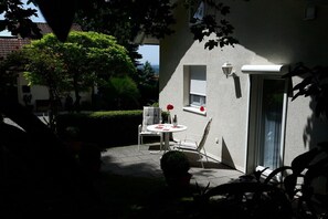 An outdoor patio with a table and chairs, a potted plant, and a view of a building with a window and a door. - Villa Maja Lake Constance (Markdorf)