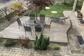 Een terras met een ronde tafel en stoelen, omgeven door een houten terras.
