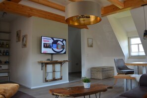 A modern living room with a television mounted on the wall, a wooden coffee table, and a seating area with a sofa and chairs. - Holiday apartment with 1 bedroom (Ellingen)