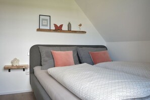Een slaapkamer met een bed, kussens, een plank met decoratieve objecten en een lijst met een foto aan de muur.