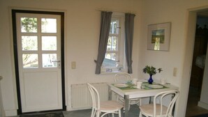 Een eetruimte met een tafel, stoelen, een vaas met bloemen, een raam met gordijnen en een deur.