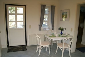 A dining area with a table, chairs, a vase with flowers, a window with curtains, and a door. - Holiday apartment with 1 bedroom (Sierksdorf)