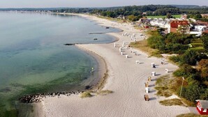 Una playa costera con una hilera de cabañas de playa, una orilla arenosa y edificios residenciales al fondo.