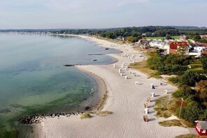 A coastal beach with a row of beach huts, a sandy shore, and a backdrop of residential buildings. - Holiday apartment with 1 bedroom (Sierksdorf)
