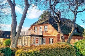 A traditional brick house with a thatched roof, a balcony, and a well-maintained garden. - Holiday apartment with 1 bedroom (Sierksdorf)
