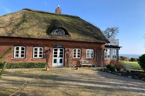 Een rieten huis met een bakstenen gevel, een houten bankje en een helder uitzicht op de zee.
