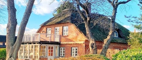 Une maison traditionnelle en briques, avec un toit de chaume, un balcon et un jardin bien entretenu.