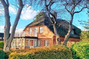 A traditional brick house with a thatched roof, a balcony, and a well-maintained garden. - Holiday apartment with 1 bedroom (Sierksdorf)