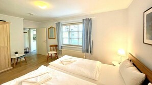Een hotelkamer met twee bedden, een raam met gordijnen, een stoel, een tafeltje en een lamp.